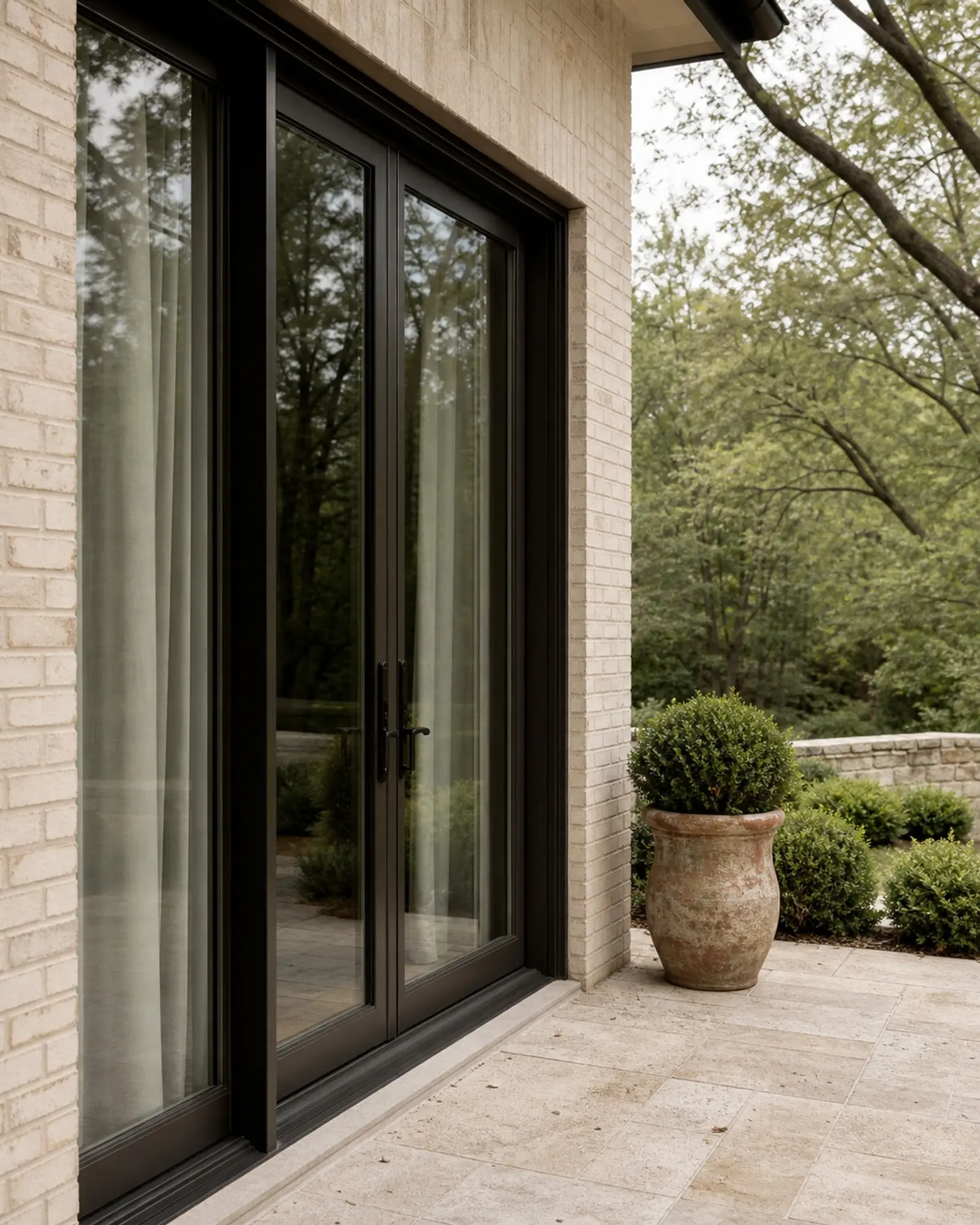 Bronze-black glazed patio doors opening to a limestone terrace and shaded garden (concept image)